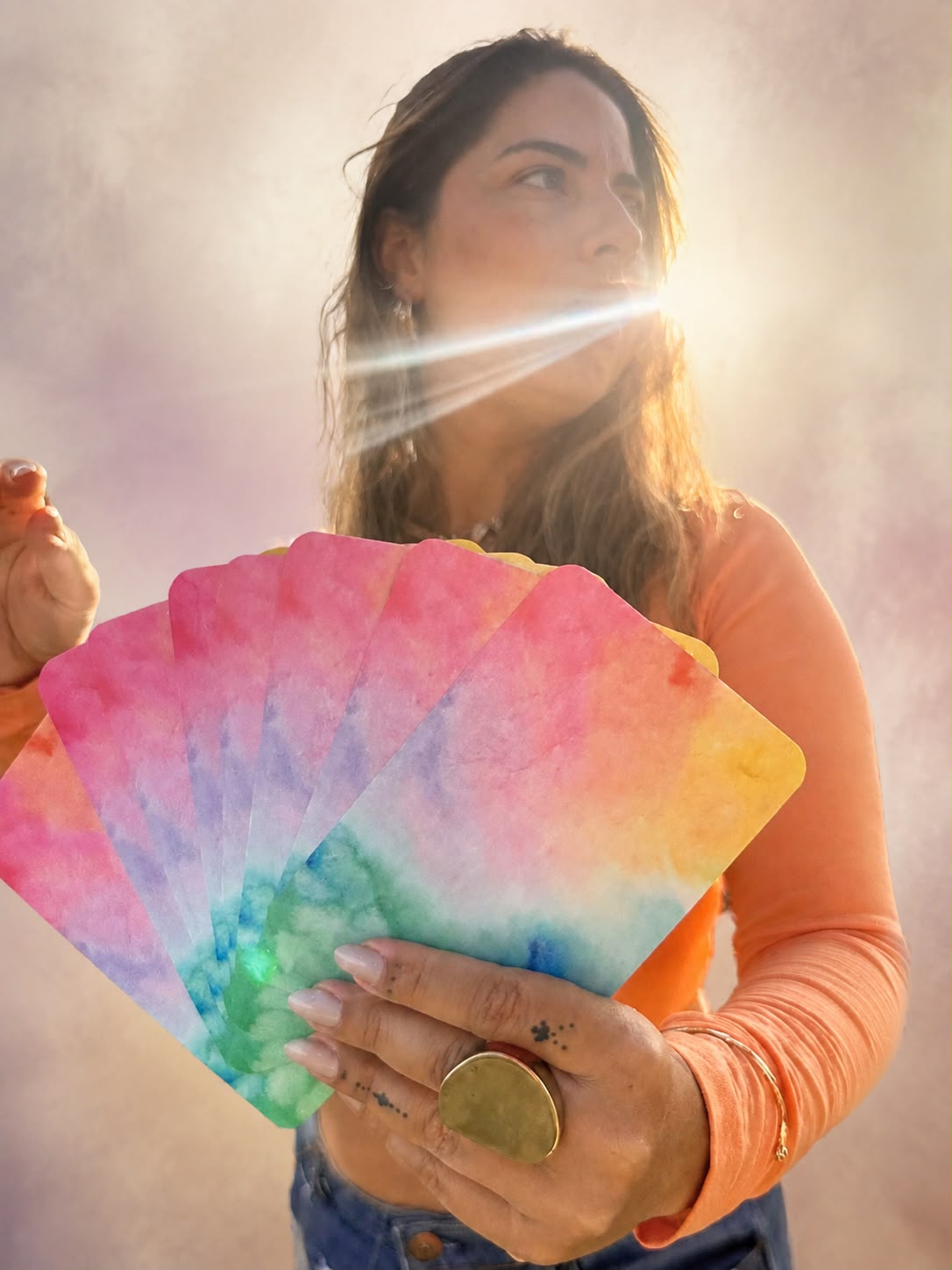 Naiara Martins ao ar livre, segurando cartas de tarot coloridas em contraluz do sol